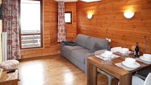 A cozy room with a wooden interior, a grey sofa, a dining table set for four, and a window with curtains. - Studio for 4 people in the heart of the resort of Les Orres 1650 (LES ORRES 1650)