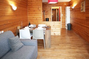 Interior de uma cabana de madeira com área de jantar, sofá e cozinha.
