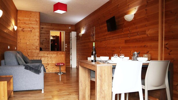 Un intérieur en bois avec un canapé, une table à manger, des chaises et une bouteille de vin.