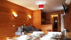 Une pièce aux murs lambrés, avec une table à manger dressée pour quatre personnes, un canapé et un miroir accroché au mur.
