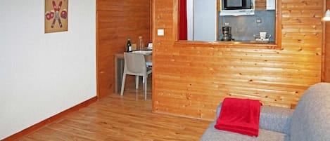 A wooden interior with a dining area, a kitchenette, and a sofa with a red blanket.
