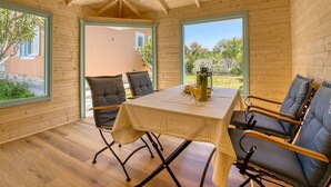 A wooden interior with a table and chairs, large windows, and a view of the outside. - Happy Home Rab by Interhome (Rab/Rab)