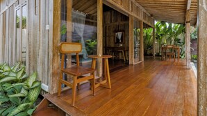 A wooden porch with a wooden chair and table, surrounded by plants and a view of the outdoors. - The Ulon Ubud Villa (Ubud)