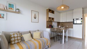 Un salon moderne avec un canapé, un coin repas doté d’une petite cuisine et un luminaire suspendu.