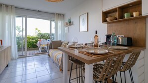 Un coin repas avec une table dressée pour quatre personnes, entouré de chaises en osier, d’un luminaire suspendu et offrant une vue sur un balcon avec une table et des chaises à l’extérieur.