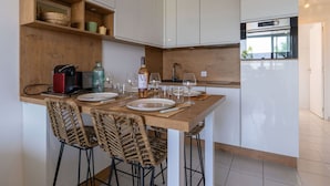 Une cuisine moderne avec des armoires blanches, un plan de travail en bois et un four encastré. On y trouve des chaises en osier et une table à manger dressée avec des assiettes et des verres.
