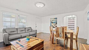 Un salon moderne avec un canapé gris, une table basse en bois et un coin repas comprenant une table et des chaises en bois.