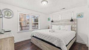 Une chambre à coucher avec un lit en bois, des murs blancs, une fenêtre avec des stores et une horloge au mur.
