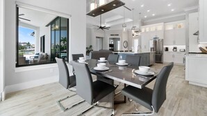 A modern kitchen with white cabinets, stainless steel appliances, and a central island. - New Construction, Immaculate Canal Home; Wide Water Views, Pool, Spa, Dock & More ~Great Location! (Marco Island)