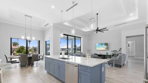 A modern kitchen with a large island, dining area, and a view of the outdoors. - New Construction, Immaculate Canal Home; Wide Water Views, Pool, Spa, Dock & More ~Great Location! (Marco Island)