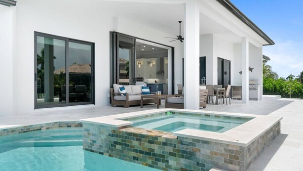 A modern house with a swimming pool, outdoor seating, and a patio area. - New Construction, Immaculate Canal Home; Wide Water Views, Pool, Spa, Dock & More ~Great Location! (Marco Island)