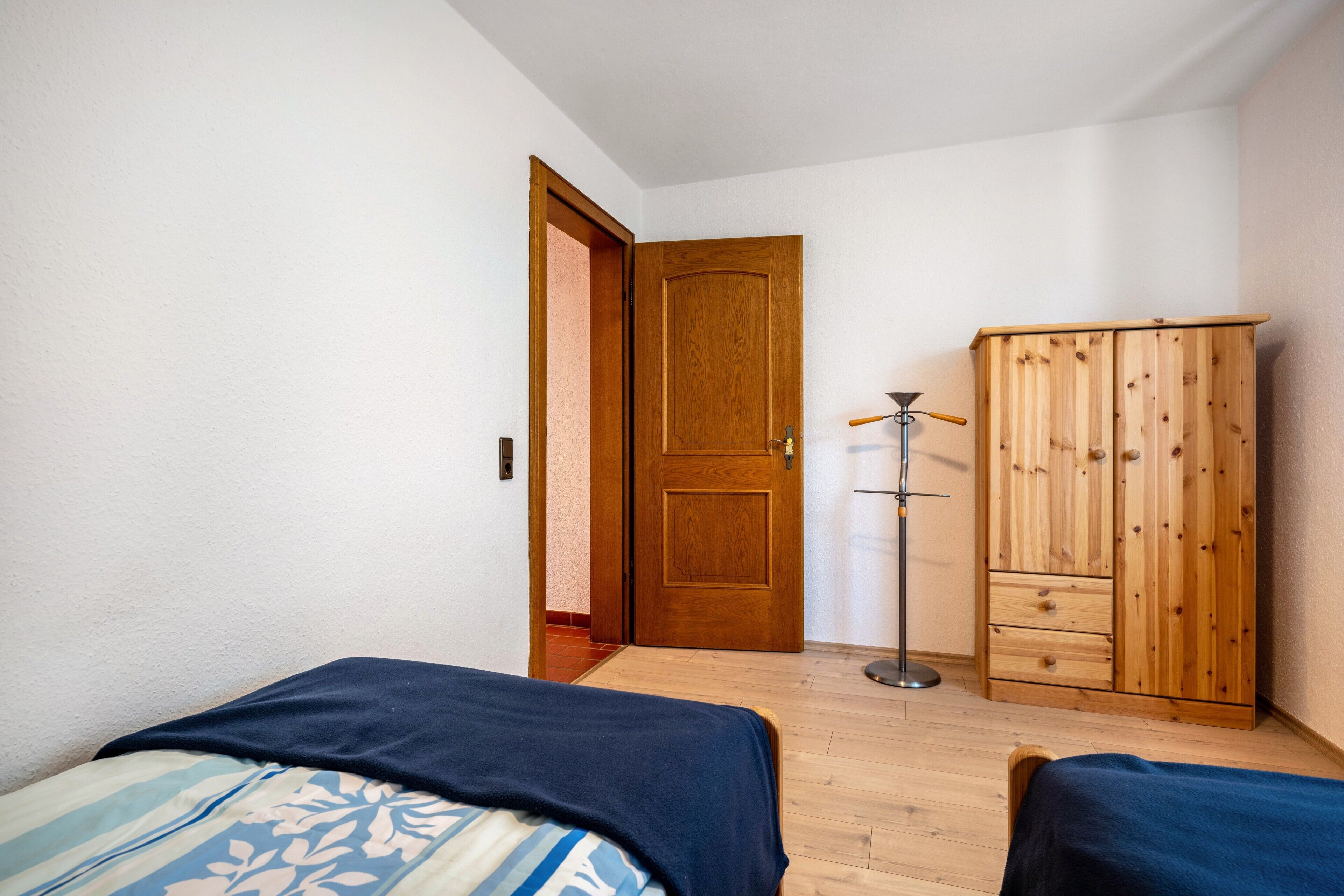 A bedroom with two beds, a wooden wardrobe, and a door.