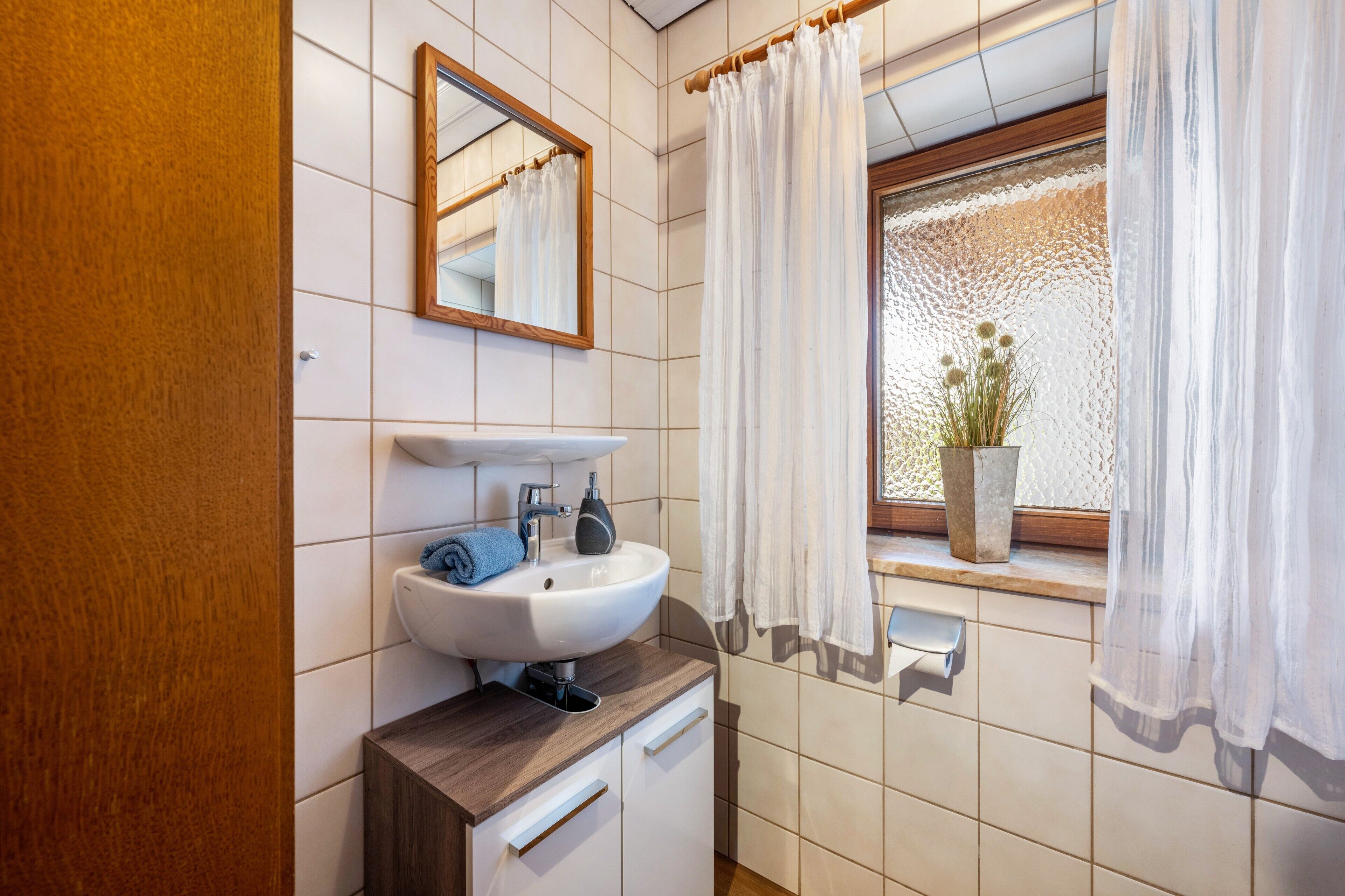 A bathroom with a white sink, wooden cabinet, and a window with a view.