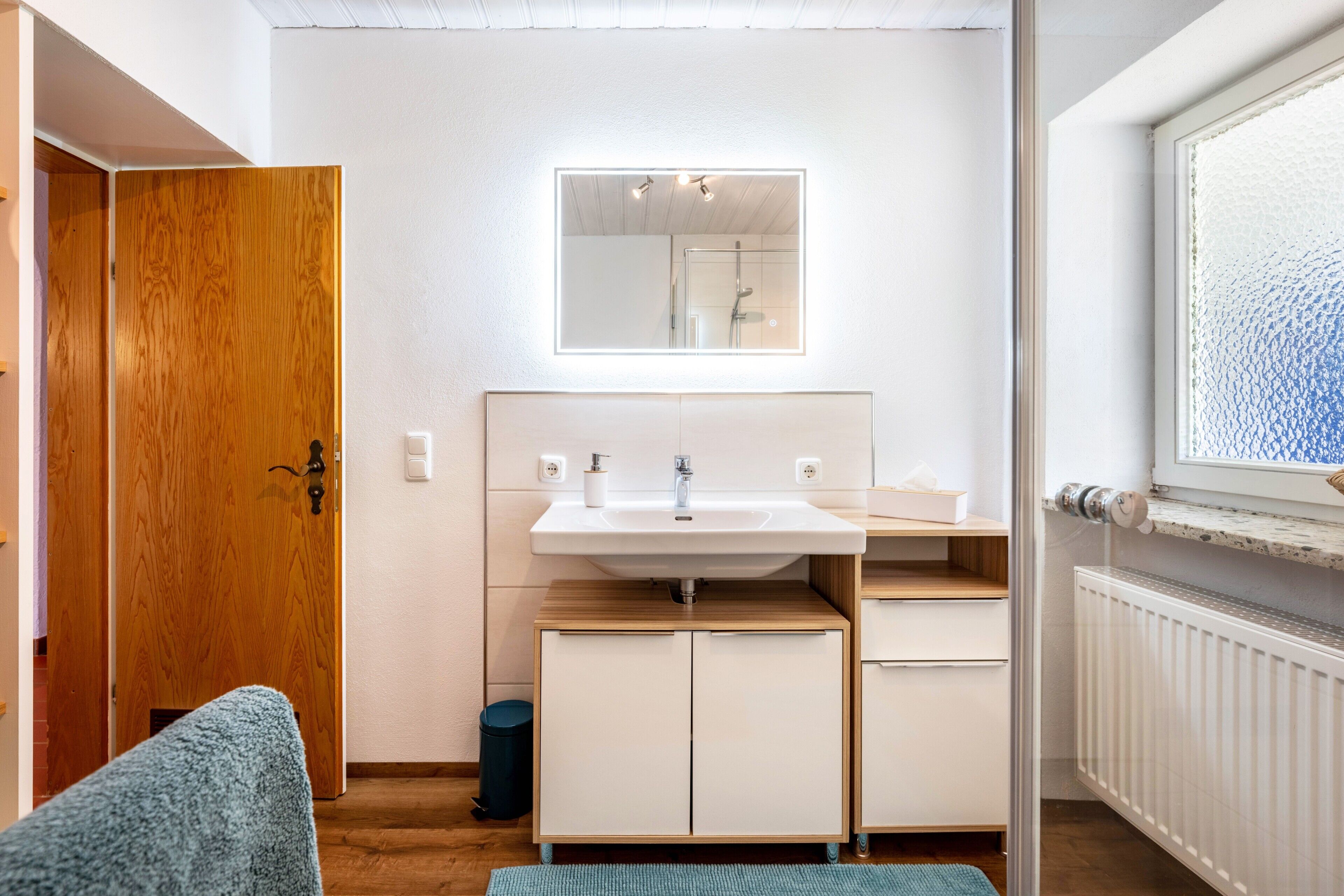 A bathroom with a wooden door, a white sink, a mirror, and a window.