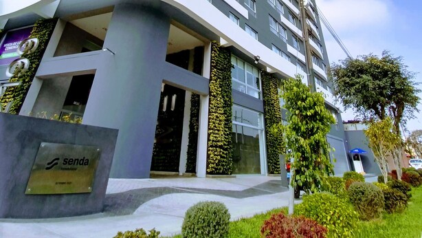 A modern high-rise building with a curved facade, multiple balconies, and a sign for 'Senda Inmobiliaria' at the base.