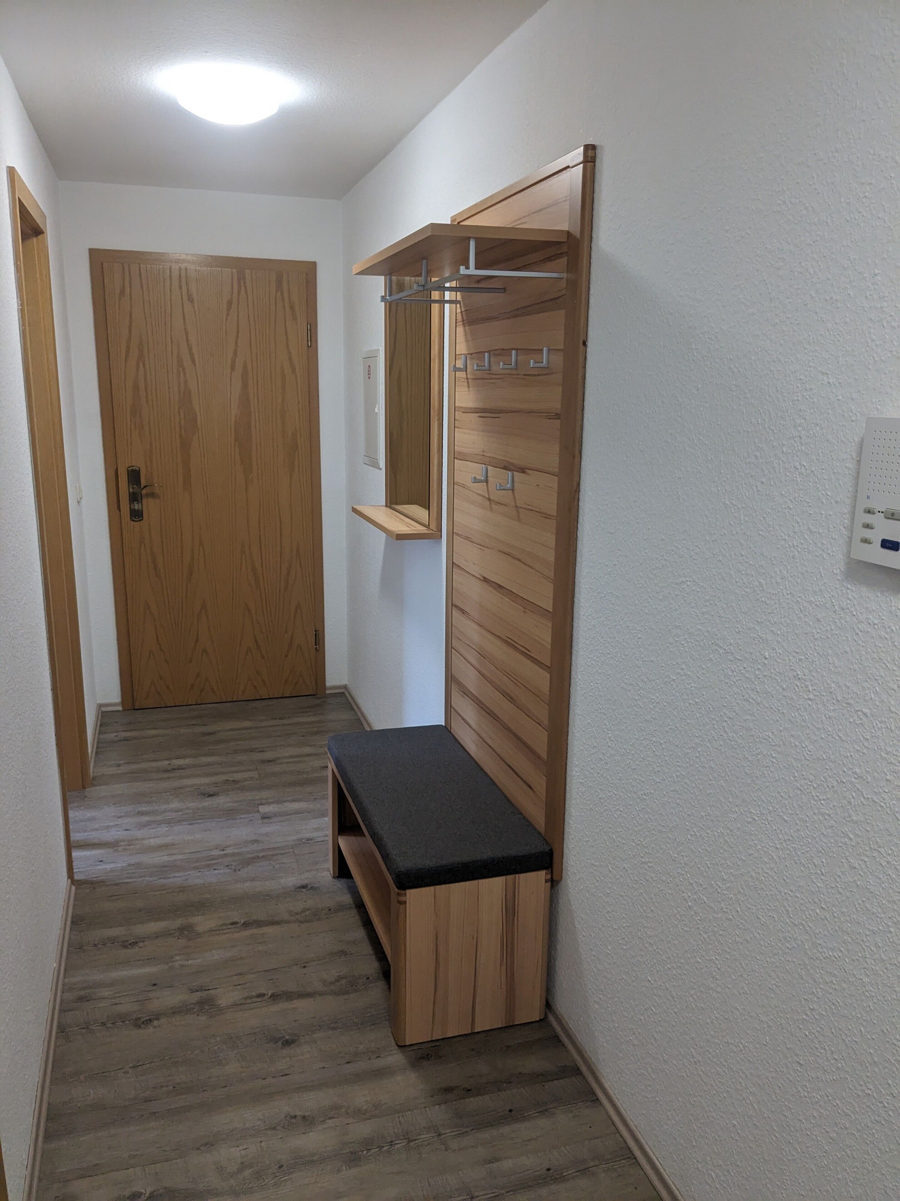 Ein Flur mit einer hölzernen Bank, einer Holztür und einem an der Wand befestigten Spiegel.