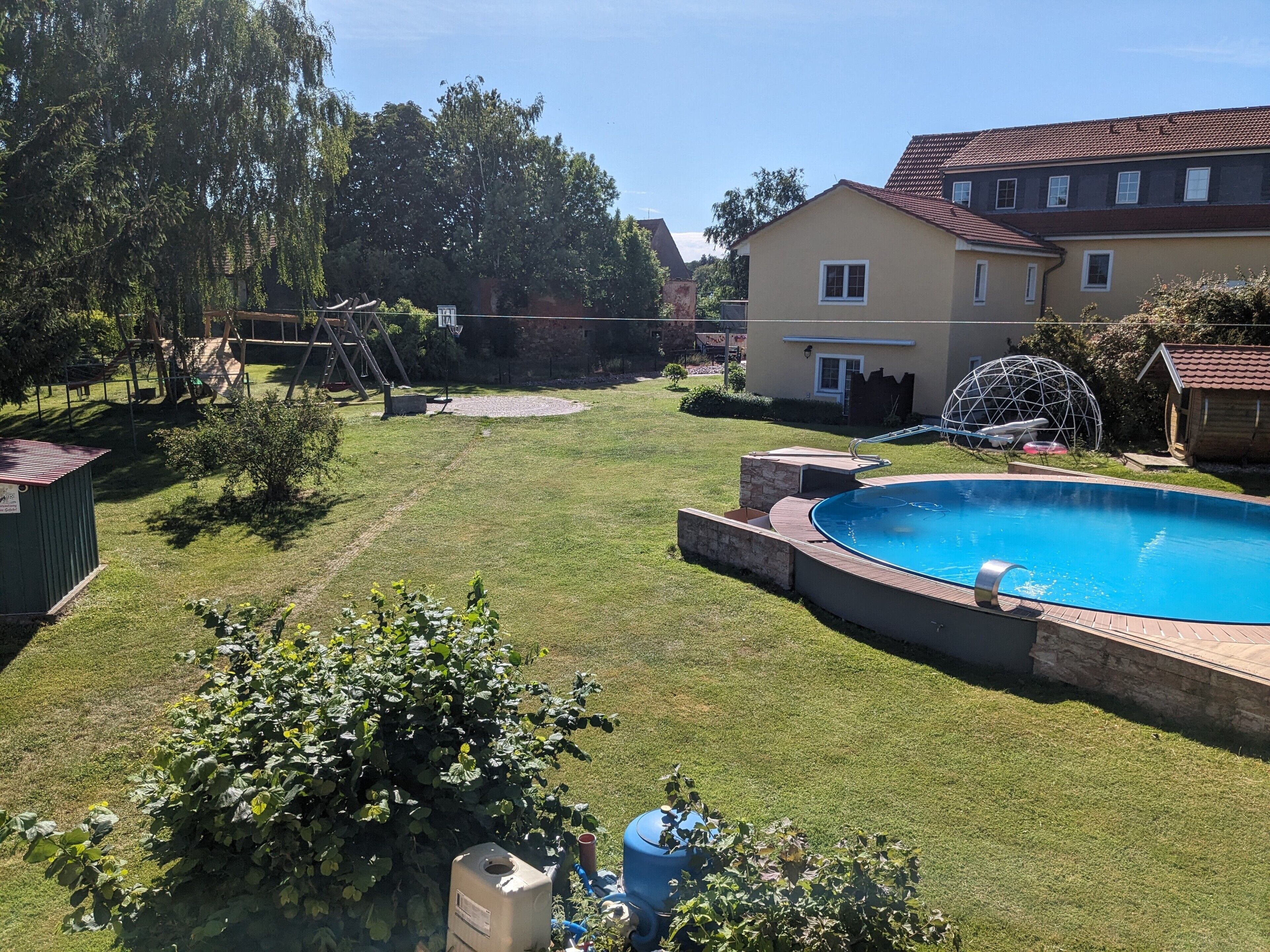 Un giardino con piscina, canestro da basket e un piccolo deposito.