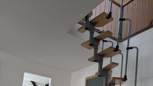 Un interior moderno con una escalera, un área de cocina visible a través de una puerta abierta y piso de madera.