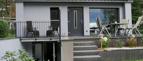 Een modern, tweelaags gebouw met een balkon, een deur en een trap naar de ingang.