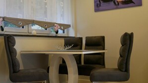 A dining area with a table and four chairs, a window with blinds, and a painting of swans on the wall. - Holiday Home 'Am Kiefernweg 17' with Private Terrace (Schwielochsee)