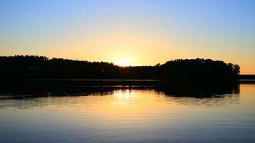 Ein ruhiger See bei Sonnenuntergang, im Vordergrund eine Baumsilhouette und ein klarer Himmel.