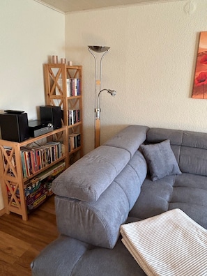 Un salón con un sofá seccional gris, una estantería de madera y una lámpara de pie.