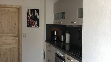 Eine Küche mit weißen Schränken, einer Holztür und einer schwarzen Arbeitsplatte.