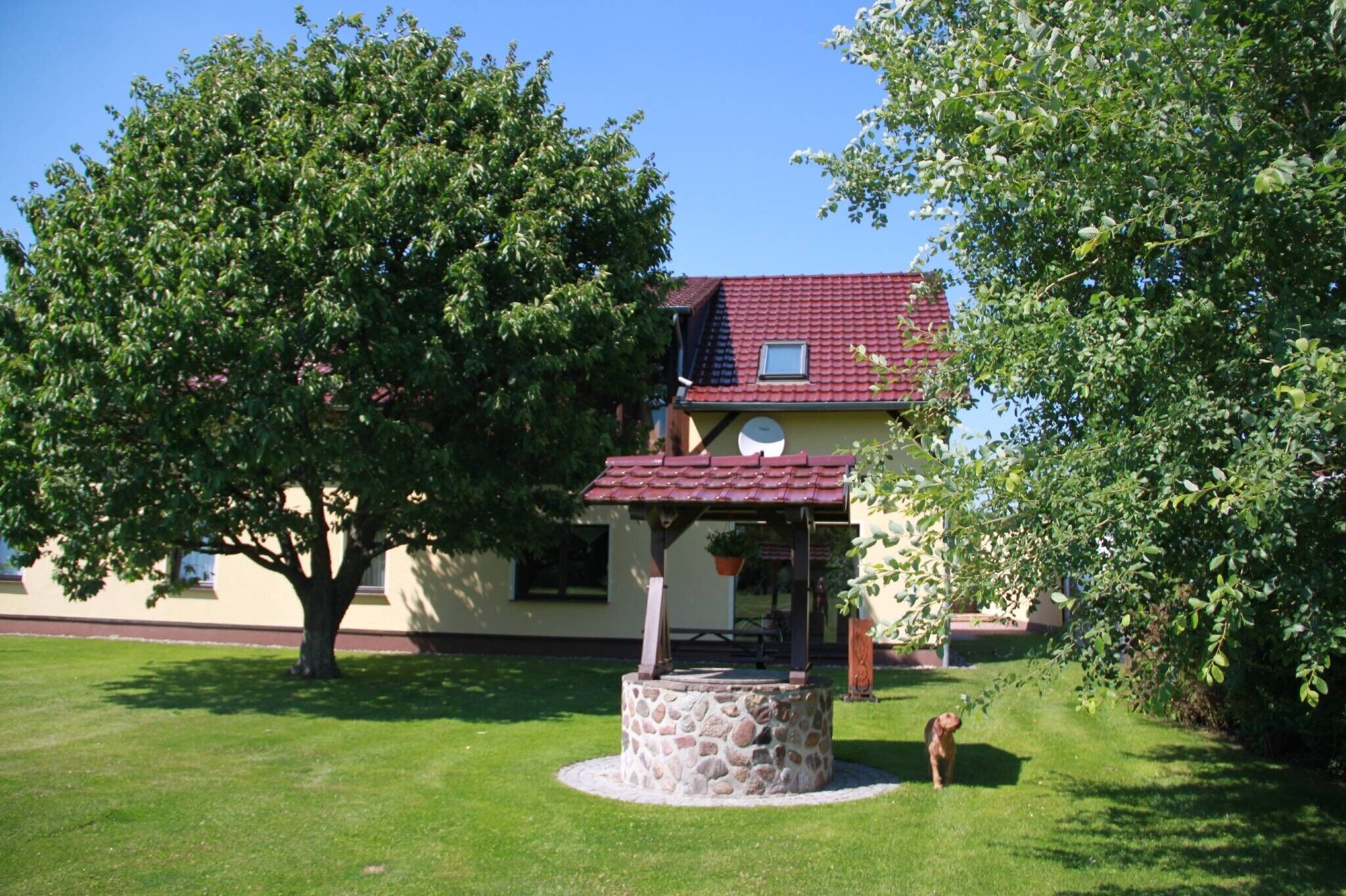 Une maison avec un puits en pierre, un toit rouge et un arbre au premier plan.