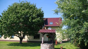 Una casa con un pozo de piedra, techo rojo y un árbol en primer plano.