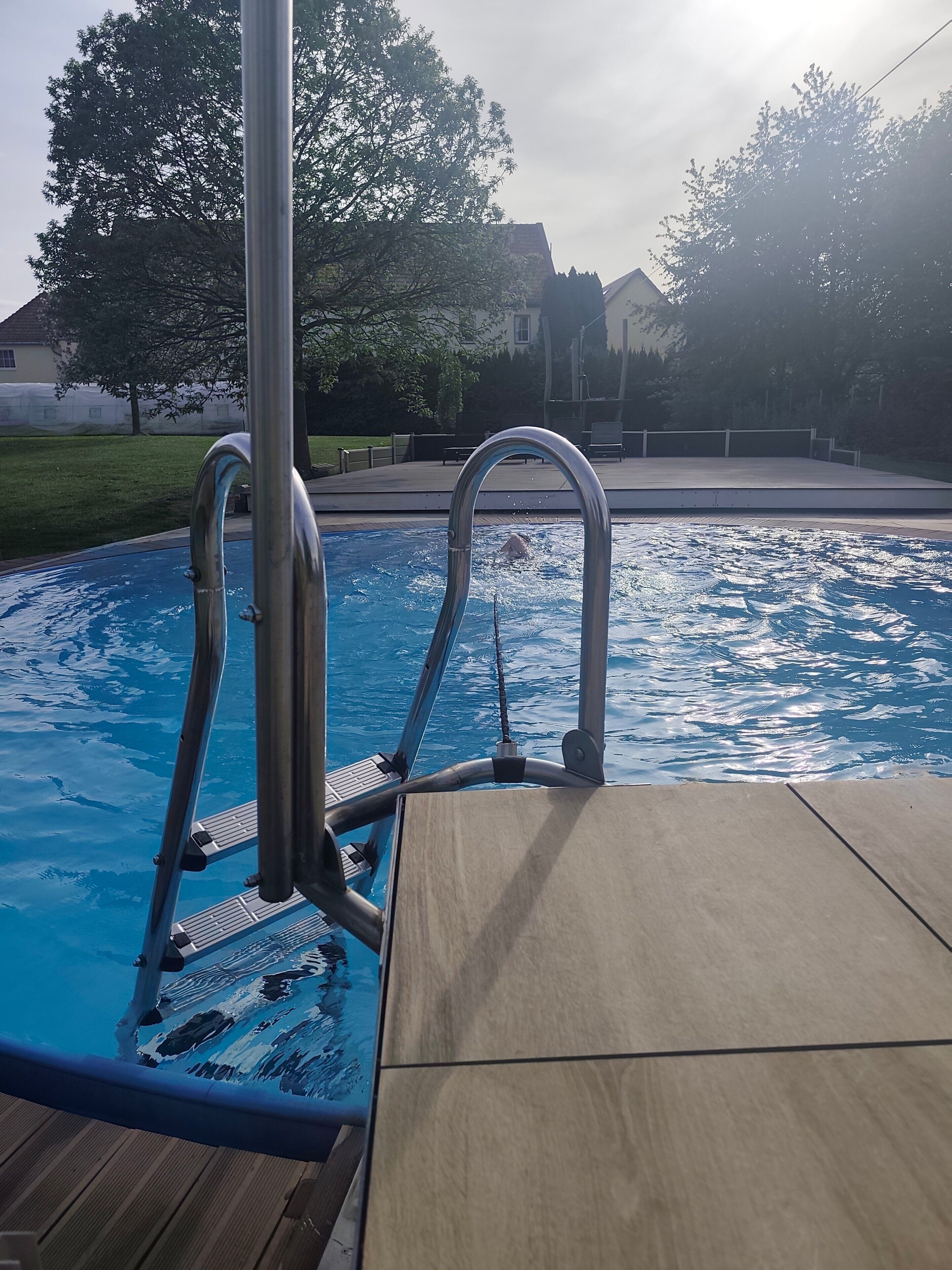 Ein Schwimmbecken mit Metallleitern und einer Holzterrasse.