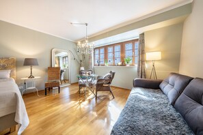 A room with a bed, a sofa, a dining table with chairs, a mirror, and a window with curtains.
