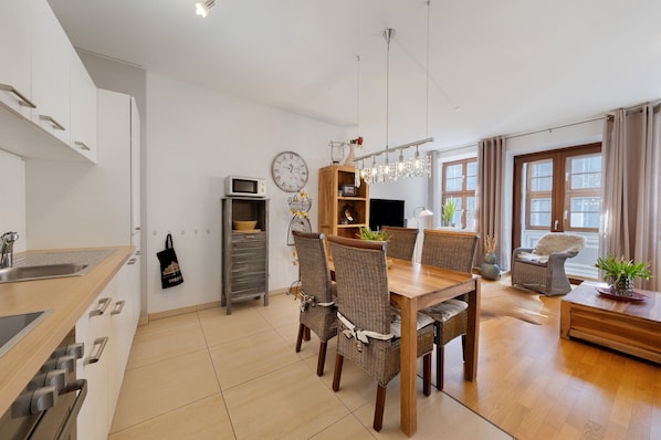 Une cuisine moderne avec une table à manger en bois, des chaises en osier, un meuble en bois et une horloge au mur.
