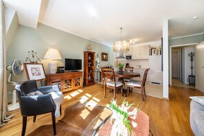 Amplia sala de estar con comedor, muebles de madera, televisor y cocina al fondo.