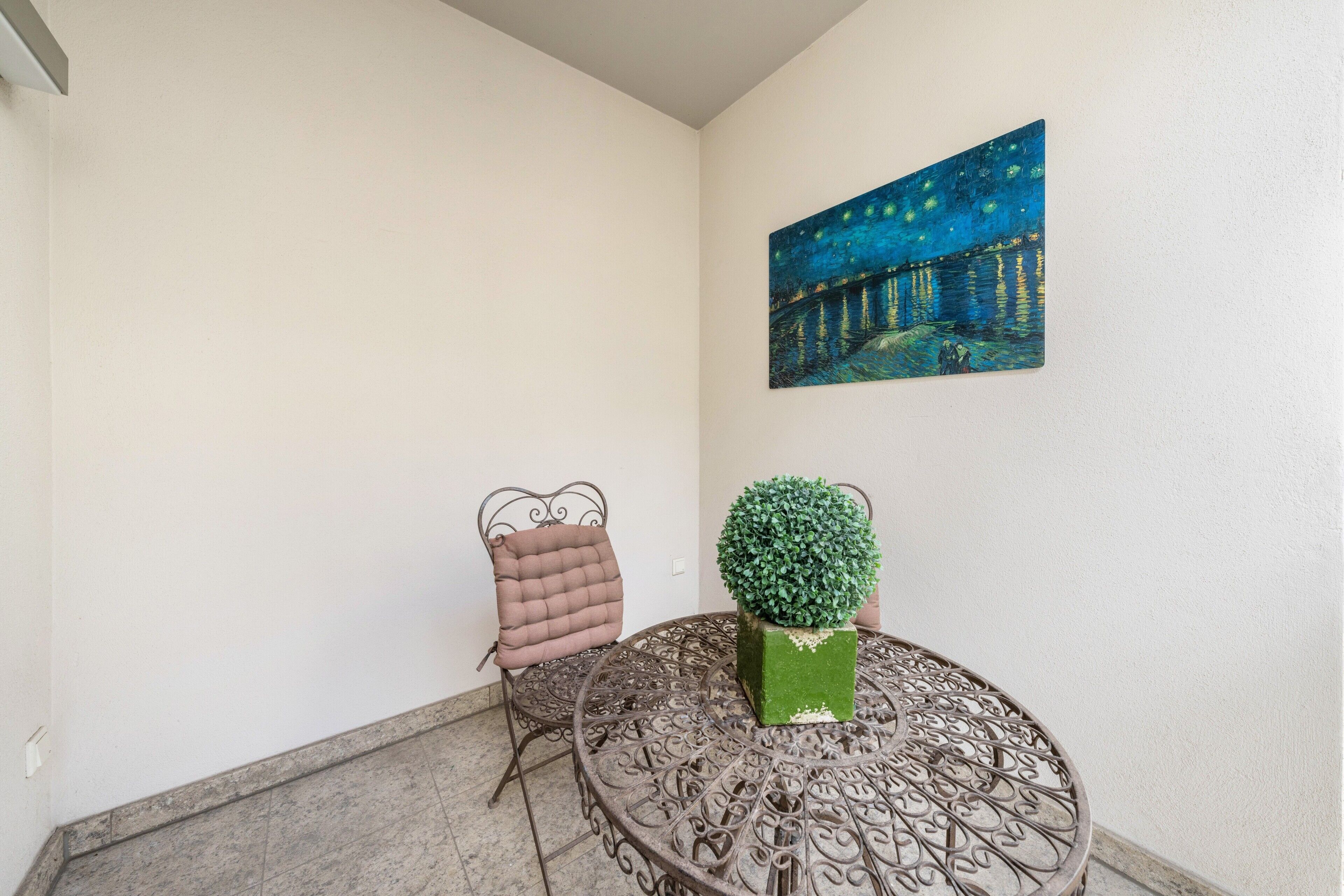 Ein Zimmer mit einem runden Metalltisch, einem gepolsterten Stuhl, einer Blumentopf-Pflanze und einem Bild an der Wand.