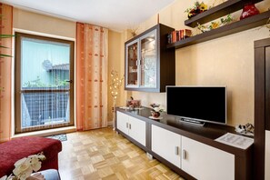 Une pièce comprenant une télévision, un meuble, une fenêtre avec des rideaux et une petite table agrémentée d’objets décoratifs.