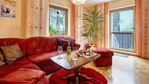 A living room with a red sofa, a table with glasses, a plant, and a balcony view.