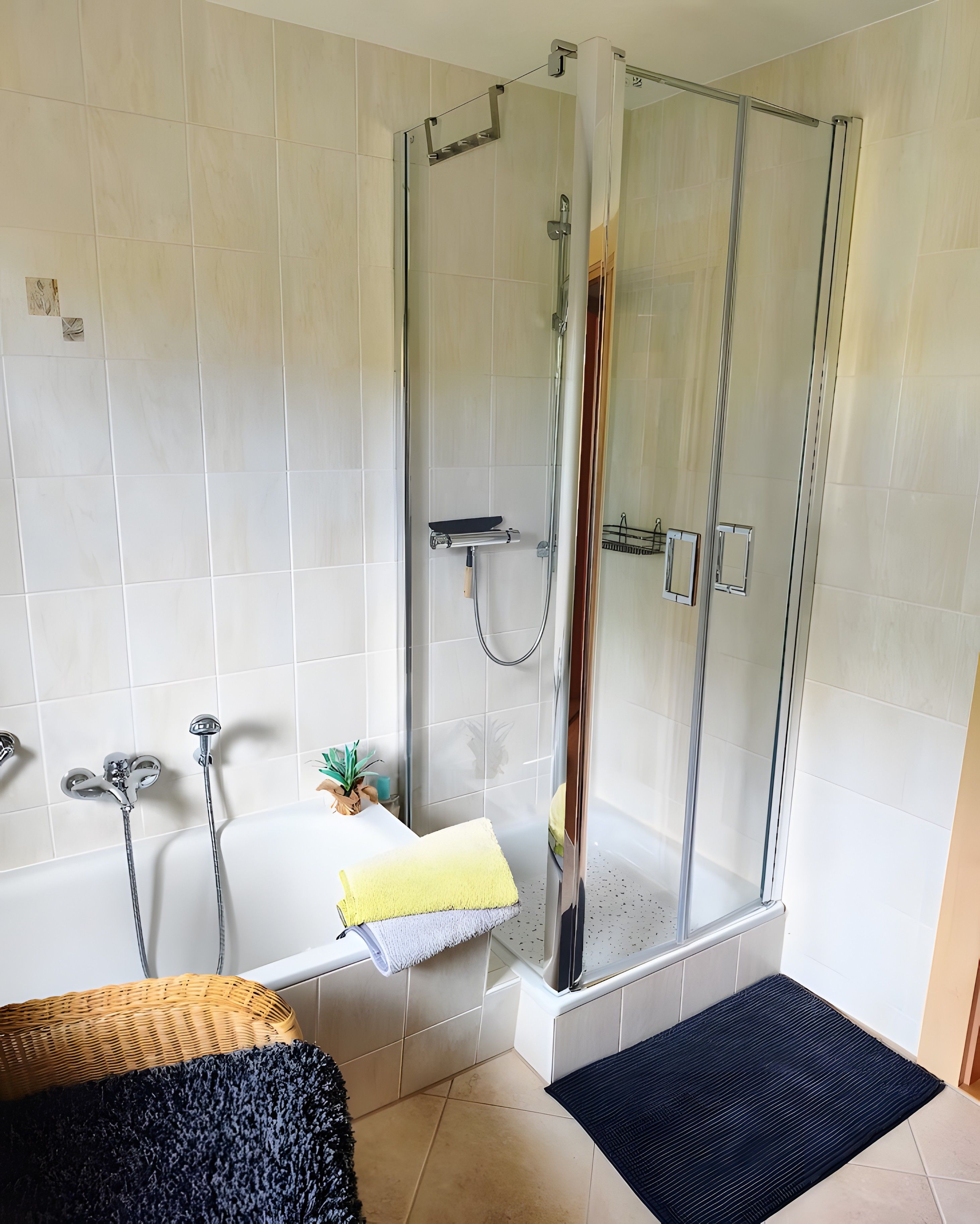A modern bathroom with a glass-enclosed shower, a bathtub, and a small potted plant.