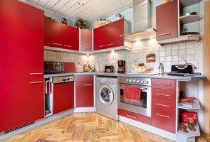Une cuisine de taille réduite avec des meubles de rangement rouges, un lave-linge, un four et une machine à café.