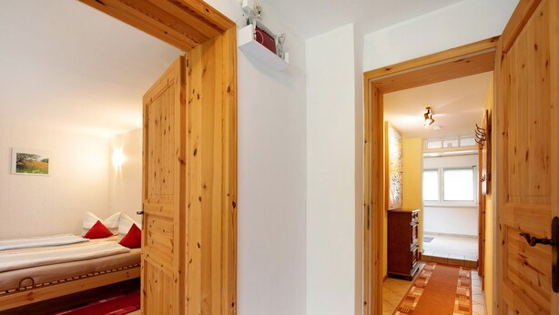 A wooden room with a bed, a red rug, and a wooden door leading to another room. - Holiday Home 'Ferienhaus Sonnenhof' with Private Terrace, Private Garden and Wi-Fi (Oberuckersee)