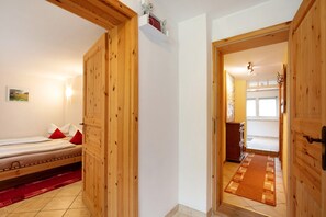 Ein Zimmer mit Holzboden, einem Bett, einem roten Teppich und einer Holztür, die in einen anderen Raum führt.
