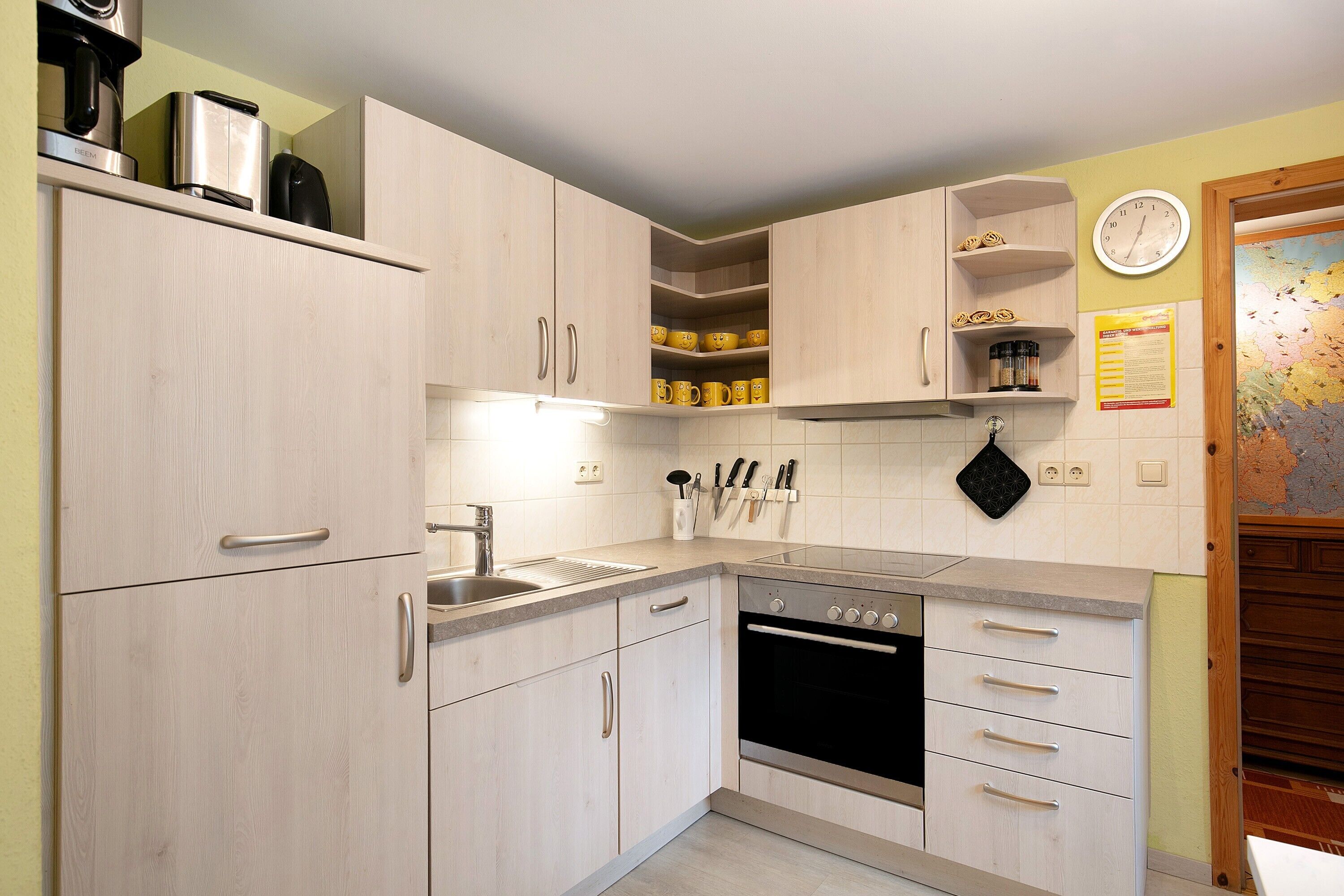 A kitchen with light wooden cabinets, a stainless steel sink, and a built-in oven.