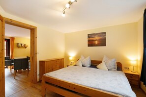 A bedroom with a wooden bed, bedside lamps, a painting on the wall, and a wooden desk with a chair.