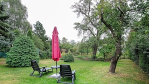 An outdoor seating area with two chairs and a table, a red umbrella, and a large coniferous tree. - Holiday Home 'Ferienhaus Sonnenhof' with Private Terrace, Private Garden and Wi-Fi (Oberuckersee)