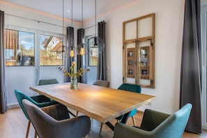 Ein moderner Essraum mit Holztisch, türkisfarbenen Stühlen und Pendelleuchten.