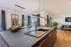 Una cocina moderna con una isla grande, electrodomésticos integrados e iluminación colgante.