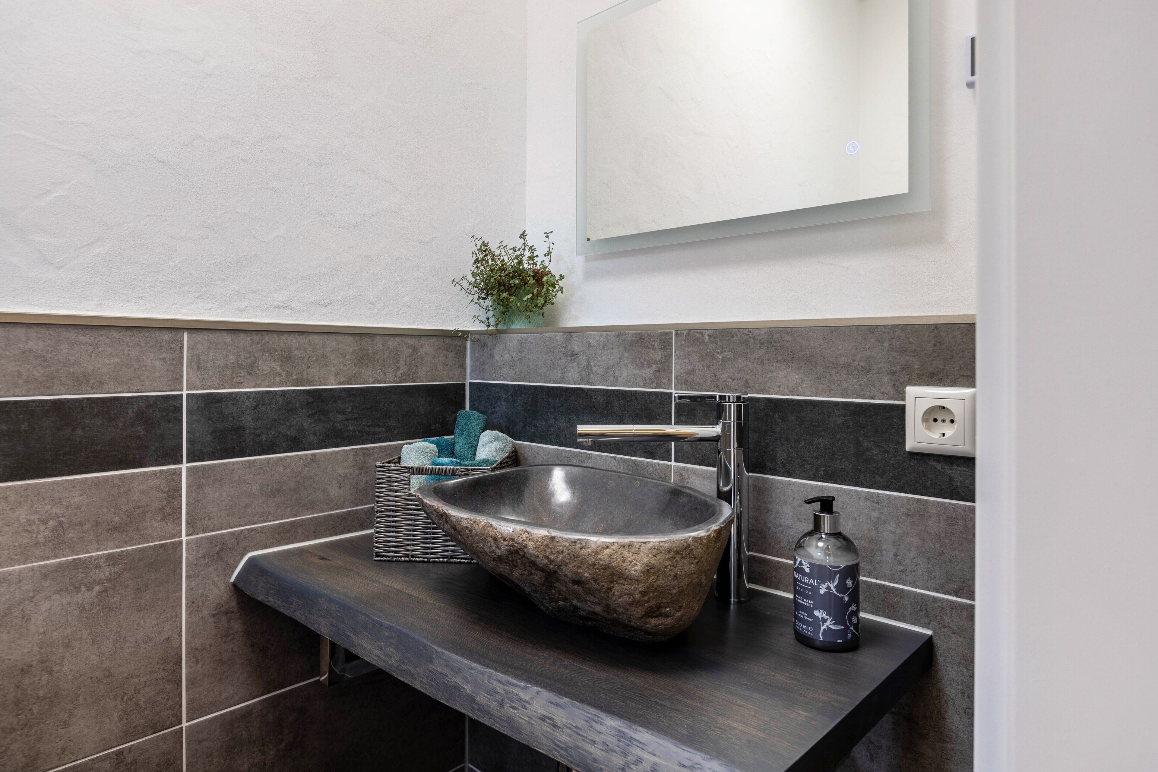 Un baño con lavamanos de piedra, un espejo, una planta y un perchero para toallas.