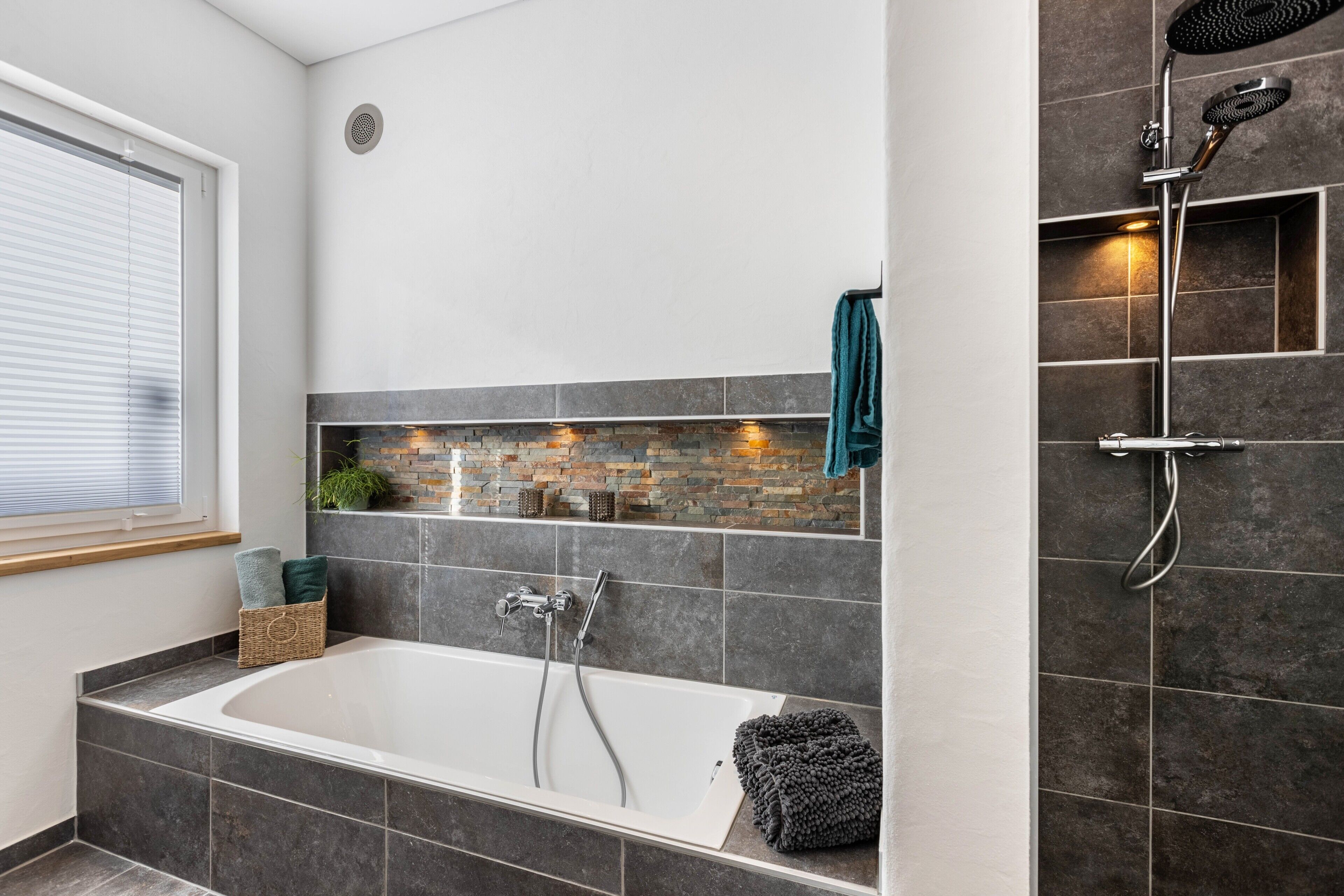 Ein modernes Badezimmer mit Badewanne, Dusche und einer Rückwand aus Stein.