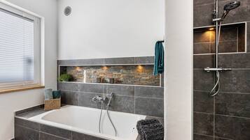 Ein modernes Badezimmer mit Badewanne, Dusche und einer Rückwand aus Stein.