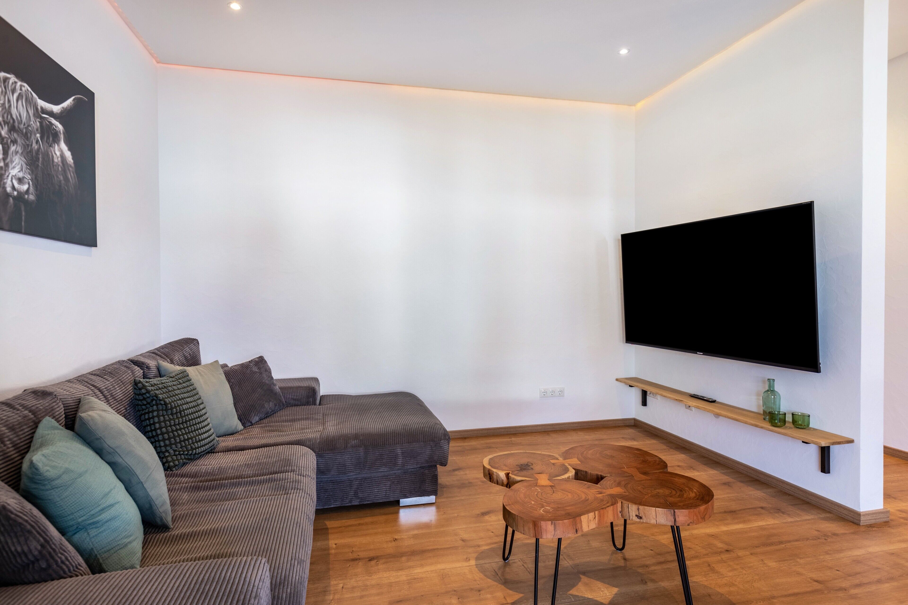 A modern living room with a sectional sofa, a flat-screen TV, wooden side tables, and a minimalist design.