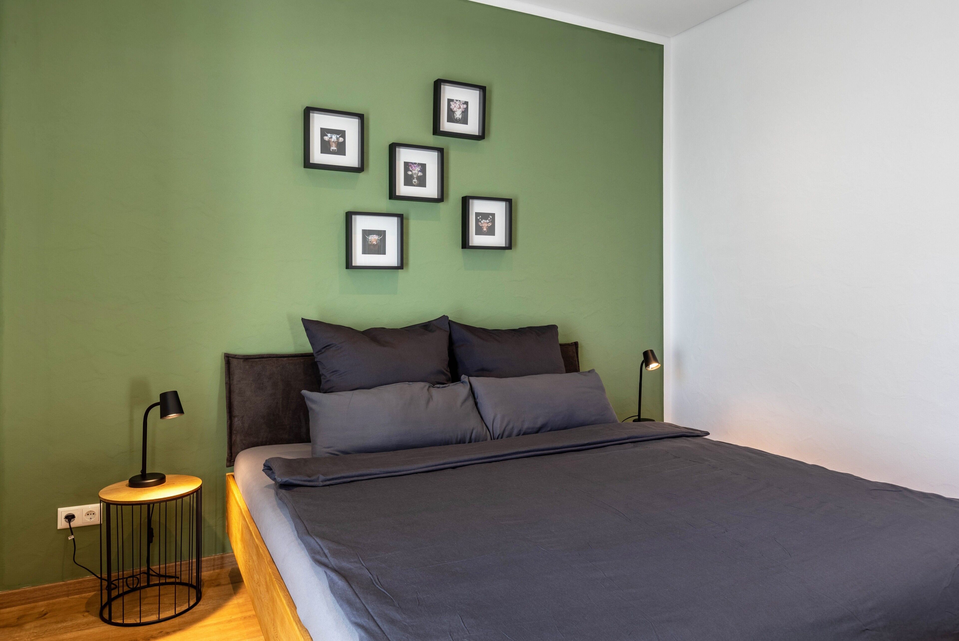 Een slaapkamer met een bed, een rond nachtkastje met een lamp en een muur met ingekaderde foto's.